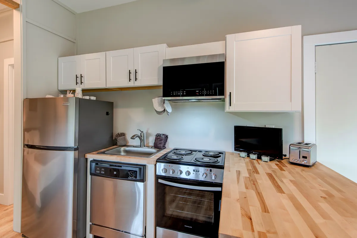 A bright, modern kitchen with stainless steel appliances, wooden countertop, and white cabinetry. The area is functional and stylish, ideal for preparing meals independently within a suite setup.