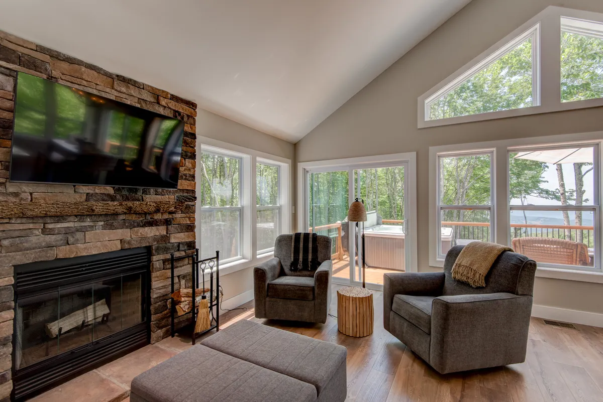 The space features a cozy seating area arranged around a stone fireplace, with large windows offering views of the mountains. The natural light and tranquil mood underscore the warmth and comfort of the great room, ideal for socializing or quiet relaxation.