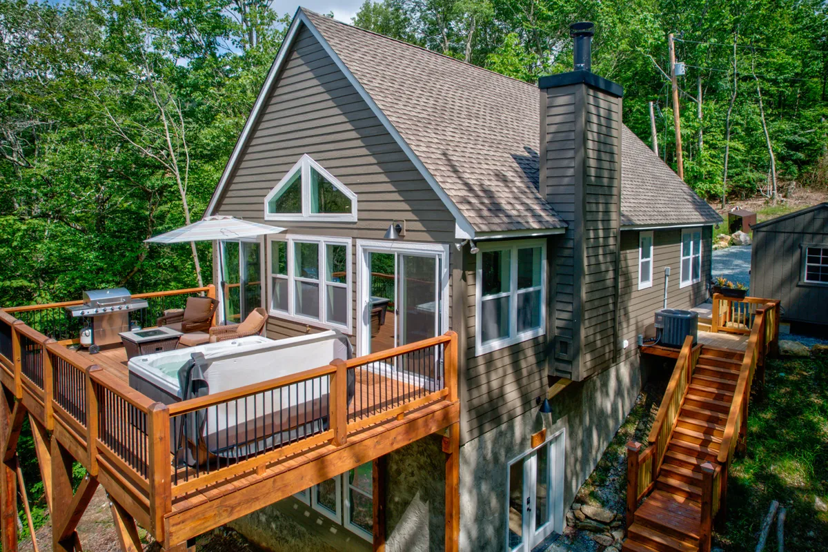 This exterior image showcases a spacious deck furnished with a large hot tub, outdoor seating area, and a gas grill set against the backdrop of open sky. The layout invites socializing and leisure, with ample space for groups to relax or dine outdoors while soaking in mountain air. The deck's design clearly supports both barbecue and hot tub experiences, aligning with several major section features.