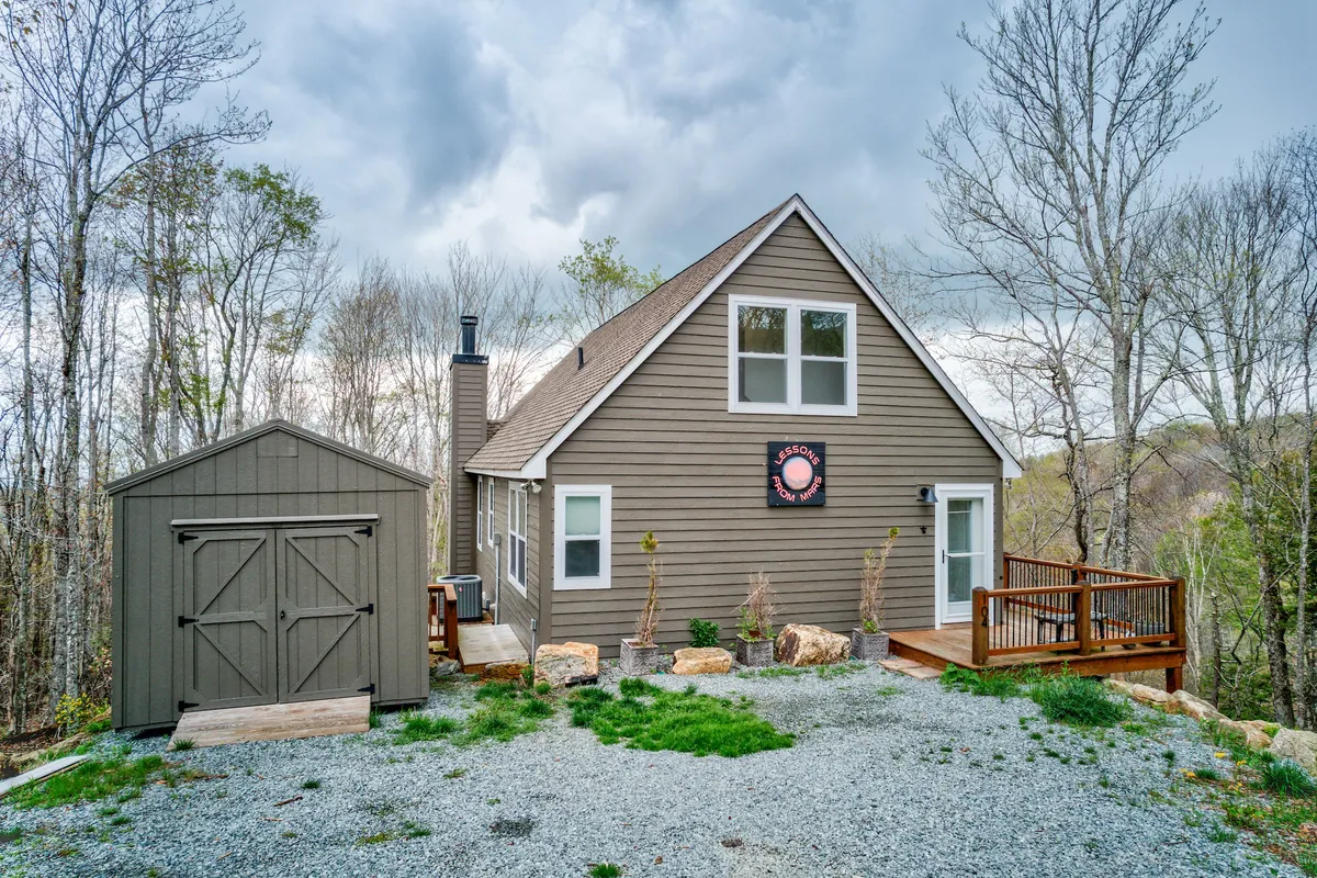 This image features the house, its spacious deck, an adjacent shed, and a welcoming garden area. The deck is set up for relaxation and outdoor dining, with ample space for both people and pets to unwind. The lush greenery and sunset lighting create a peaceful, inviting setting.