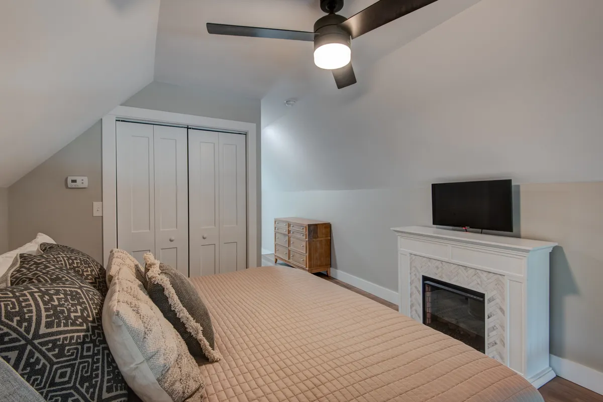 A cozy bedroom featuring a bed with decorative pillows, a fireplace for warmth and ambiance, a television, and a wooden dresser—creating a comfortable and intimate retreat perfect for relaxation.