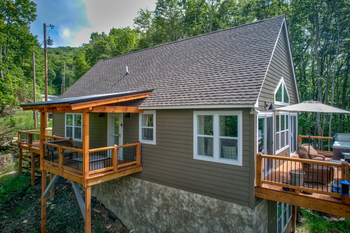 This image shows a wooden deck with outdoor seating overlooking a serene wooded area. Large windows connect the outdoor deck to the interior, highlighting the seamless transition between indoor relaxation and outdoor exploration.