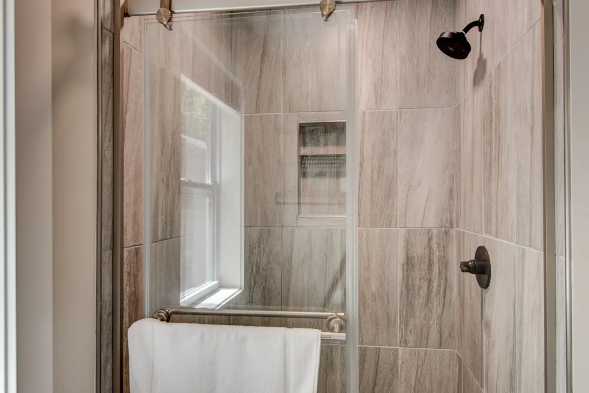A modern shower enclosure with sleek glass doors, fluffy towel, and rainfall shower head, set against clean tiled walls, evoking a spa-like atmosphere for rejuvenation.