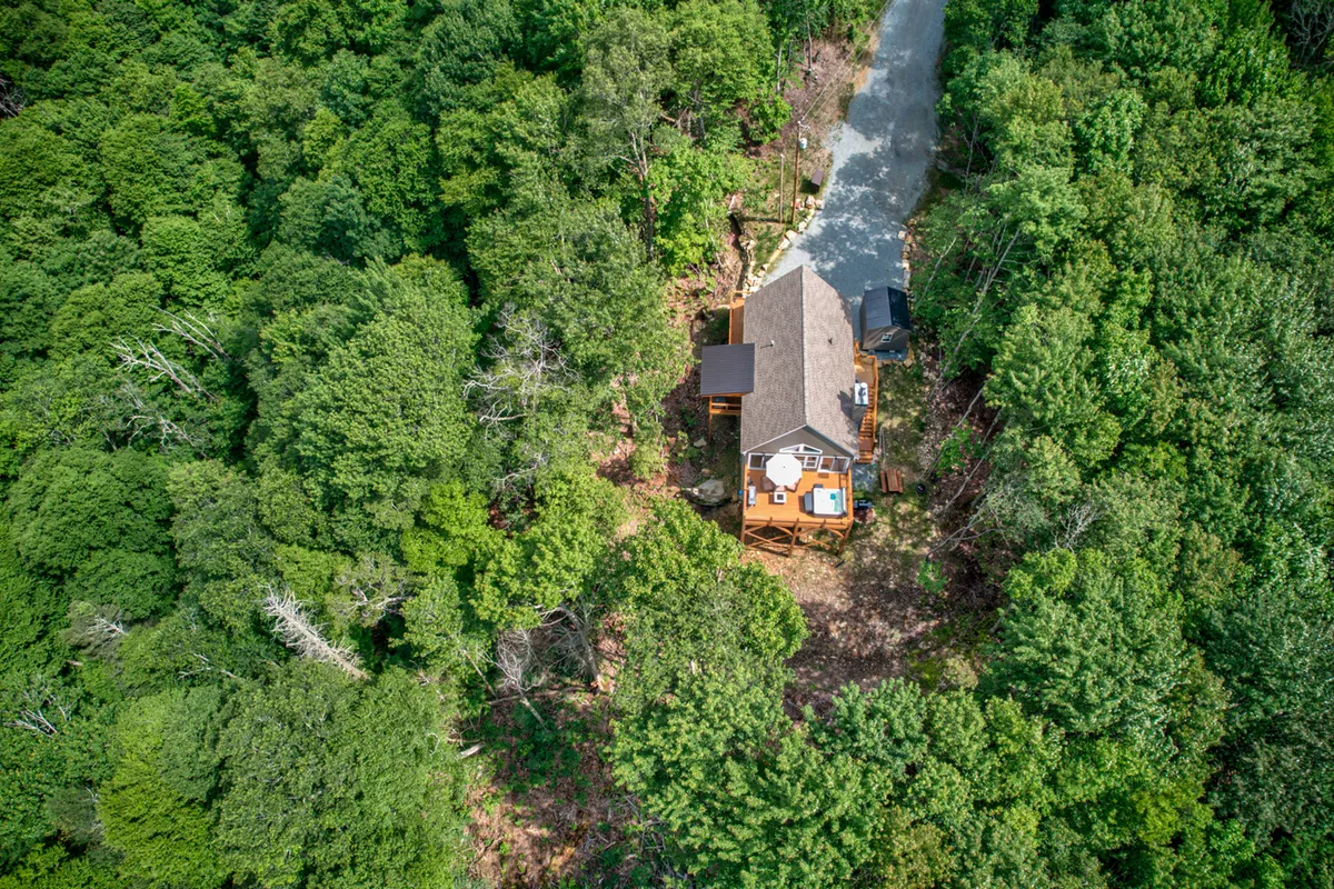 A welcoming exterior shot of the wooden mountain house set among trees, featuring a spacious deck, driveway, and a peaceful sunset-lit atmosphere. The deck is perfect for family gatherings, barbecues, and enjoying the mountain setting.