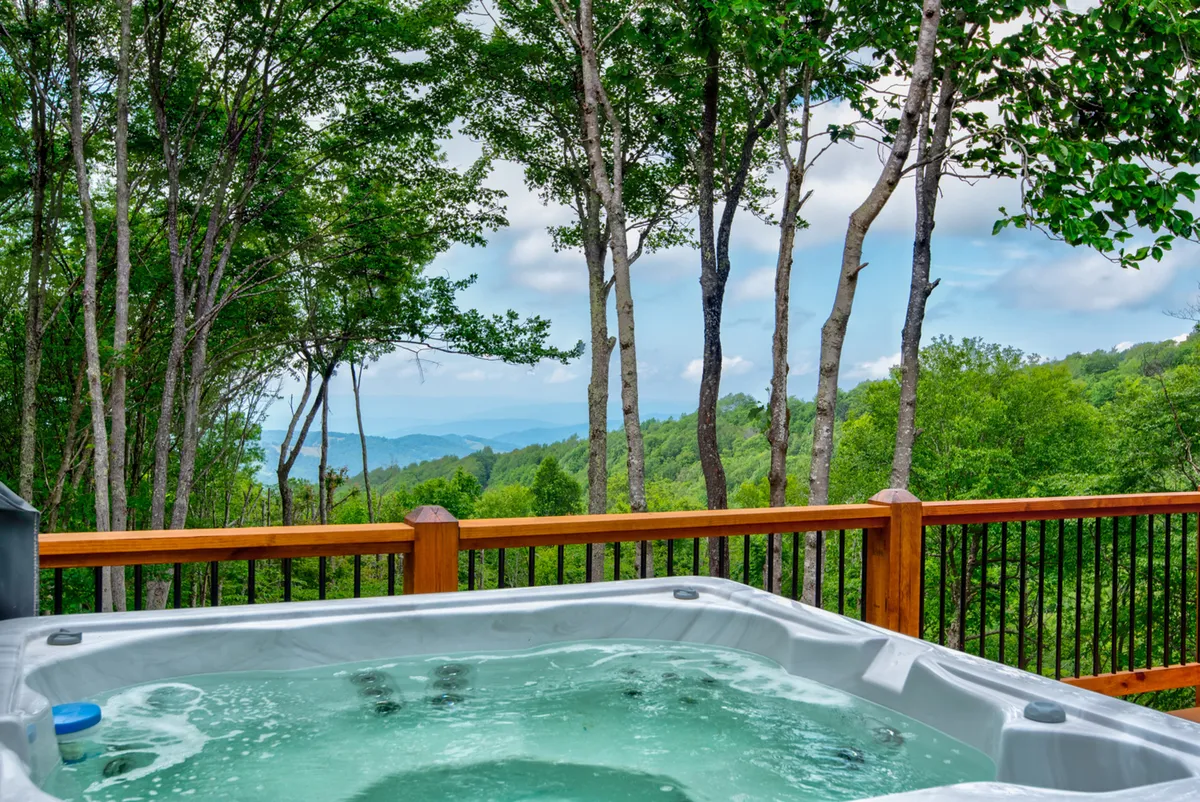 A hot tub takes center stage on a tranquil deck, framed by sweeping mountain views and lush greenery. The scene reflects a peaceful escape, perfect for unwinding after a day on the slopes or stargazing beneath the clear alpine sky. The mountain panorama underscores the property's unique alpine setting.
