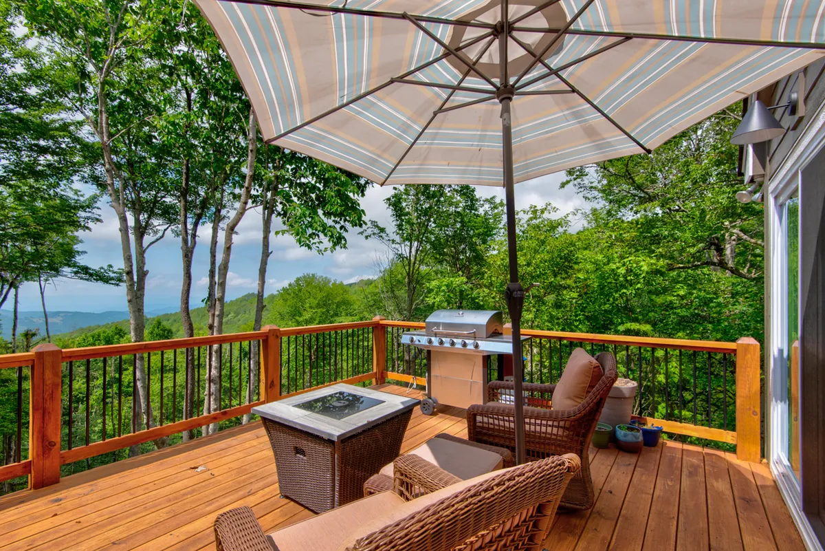 An inviting outdoor seating area with a grill and parasol sits on the deck, overlooking sweeping landscape views. This versatile setup hints at sunset barbecues, morning coffee sessions, and social gatherings, while the landscape view ties back to the mountain air and year-round enjoyment mentioned in the section.